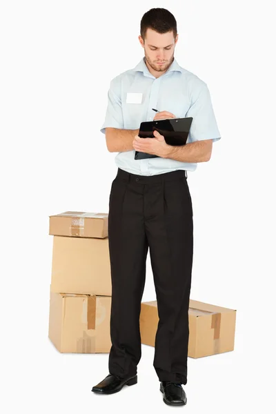 Junger Post-Mitarbeiter mit Paketen, die Notizen auf seinem Klemmbrett machen — Stockfoto
