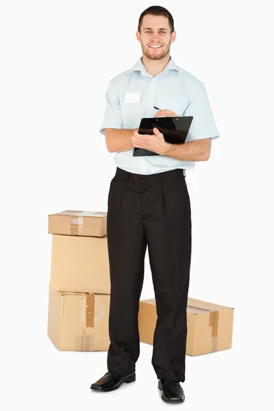 Sonriente joven empleado de correos con paquetes y portapapeles —  Fotos de Stock