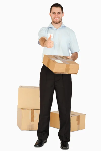 Sonriente joven empleado de correos con paquetes dando pulgar hacia arriba — Foto de Stock