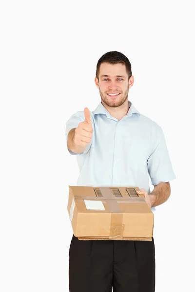 Smiling young post employee handing over parcel while giving thu — Stock Photo, Image