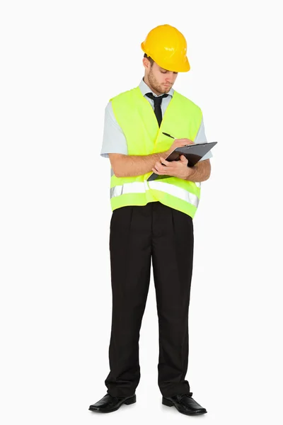 Young foreman in safety jacket taking notes on clipboard — Stock Photo, Image