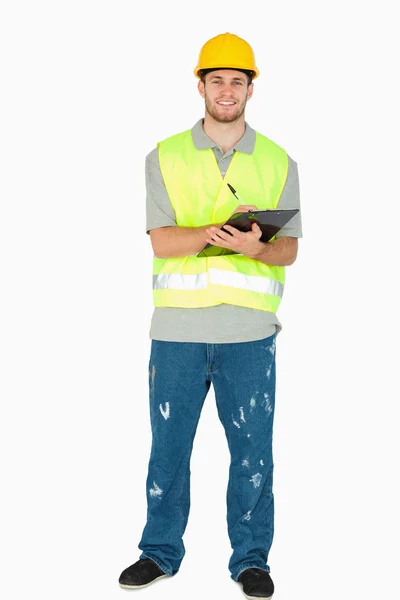 Jovem trabalhador da construção sorrindo tomando notas — Fotografia de Stock