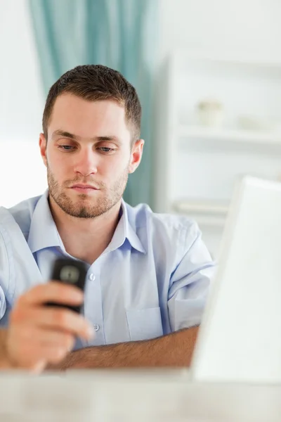 Affärsman SMS på sin mobiltelefon som sitter bakom sitt skrivbord — Stockfoto