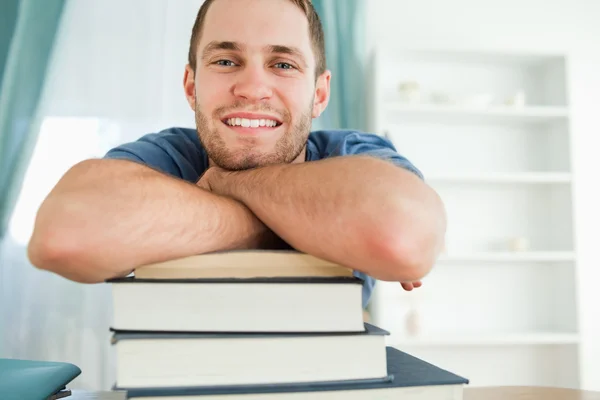 Estudante sorrindo se apoiando em uma pilha de livros — Fotografia de Stock