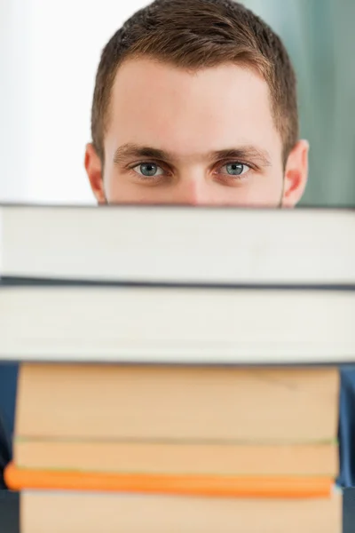 Primer plano del estudiante escondido detrás de una pila de libros — Foto de Stock