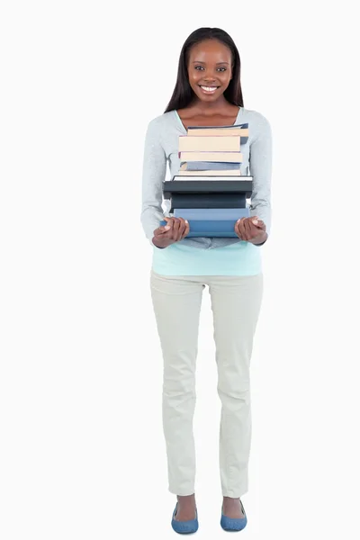 Усміхнена молода жінка, що носить стопку книг — стокове фото