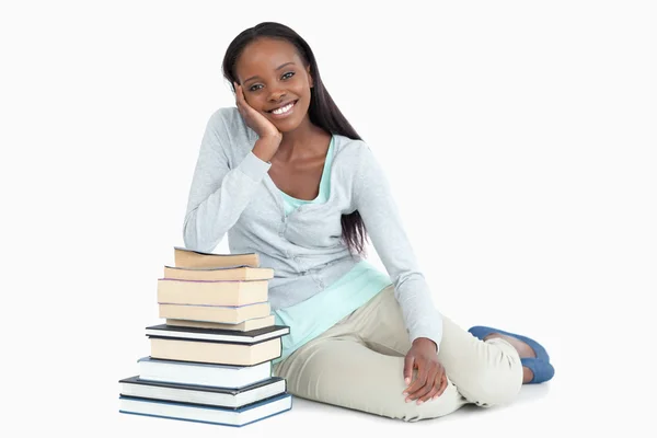 Lachende jonge vrouw leunend tegen een stapel boeken — Stockfoto