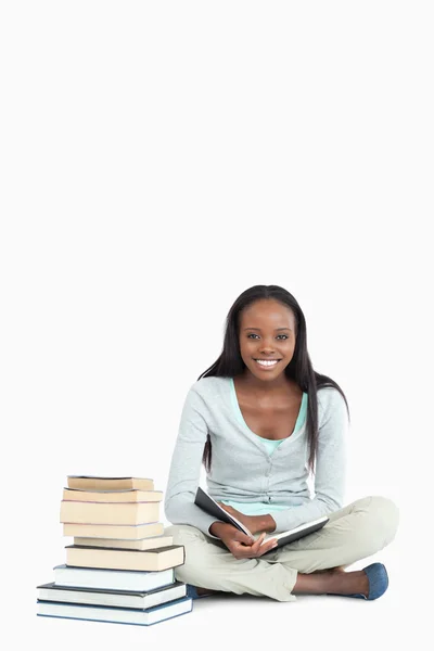 Glimlachend jonge vrouw zat naast een stapel boeken — Stockfoto