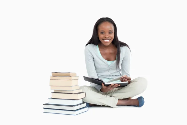 Uśmiechnięta kobieta siedząca obok stos książek — Zdjęcie stockowe