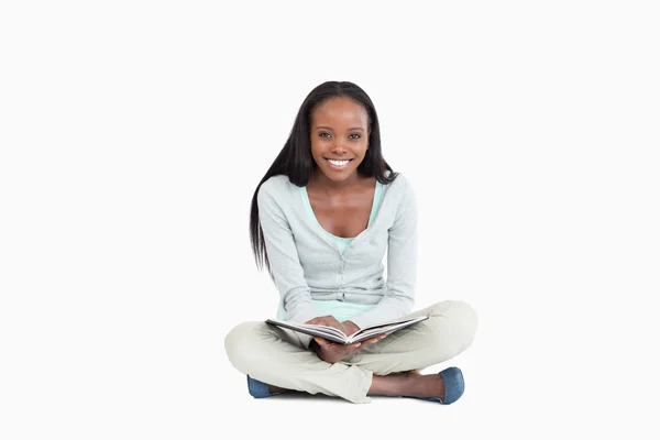 微笑着的年轻女子坐在地上拿着一本书 — 图库照片