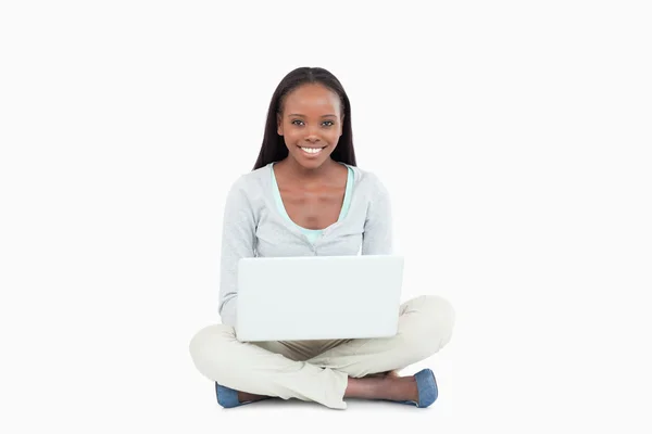 Leende ung kvinna sitter på golvet med sin laptop — Stockfoto