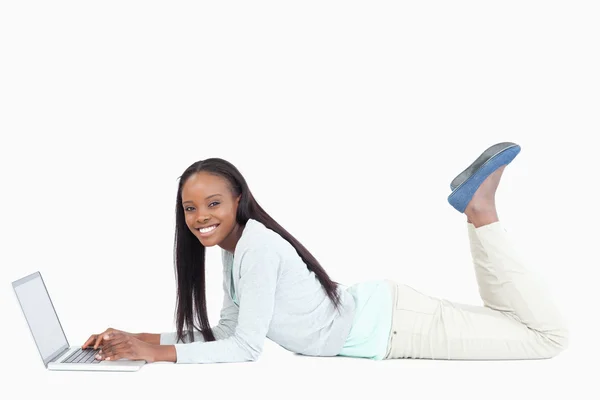 Side view of smiling woman lying on the floor with her laptop — Stock Photo, Image
