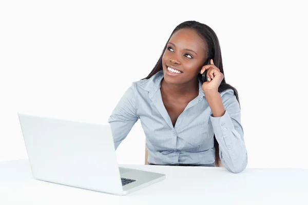 Bir dizüstü bilgisayar kullanırken telefonla iş kadını gülümseyen — Stok fotoğraf