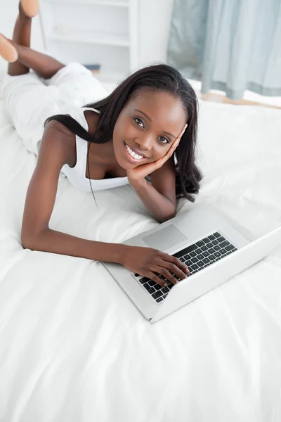Bir dizüstü bilgisayar kullanarak karnı üzerinde yatan genç bir kadın portresi — Stok fotoğraf