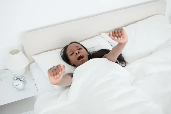 Giovane donna sbadigliando e allungando le braccia mentre si sveglia — Foto Stock