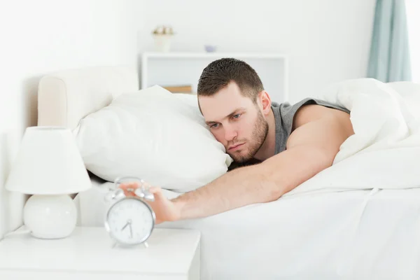 Exhausted man switching off his alarm clock — Stock Photo, Image