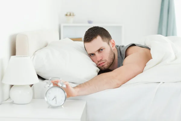 Tired young man switching off his alarm clock — Stock Photo, Image
