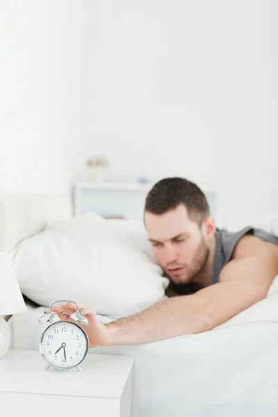 Portrait of a tired man being awakened by an alarm clock — Stock Photo, Image