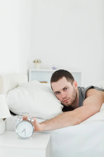 Portrait of a handsome man being awakened by an alarm clock — Stock Photo, Image