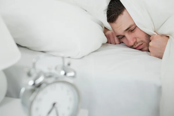 Young man covering his ears while his alarm clock is ringing — Stock Photo, Image