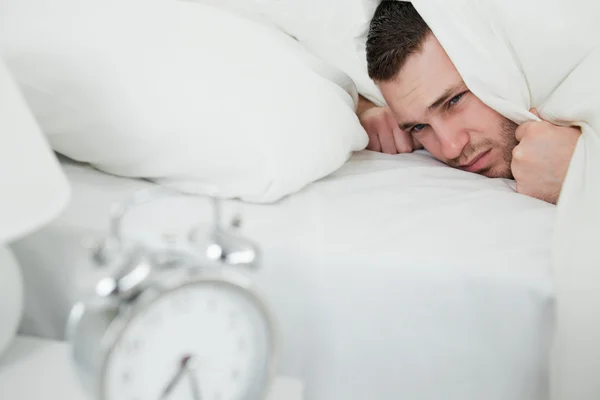 Tired man covering his ears while his alarm clock is ringing — Stock Photo, Image