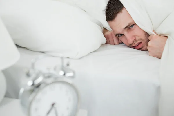 Annoyed man covering his ears while his alarm clock is ringing — Stock Photo, Image