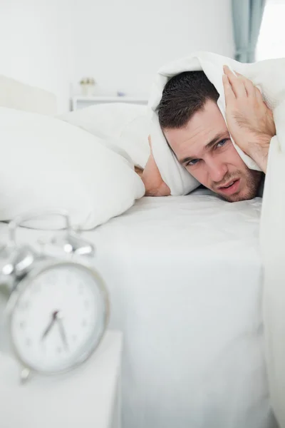 Porträt eines Mannes, der seine Ohren mit einer Bettdecke bedeckt, während sein Wecker klingelt — Stockfoto