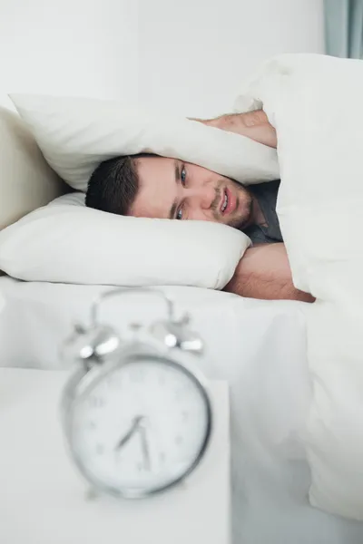 Portrait of a tired young man covering his ears while his alarm — Stock Photo, Image