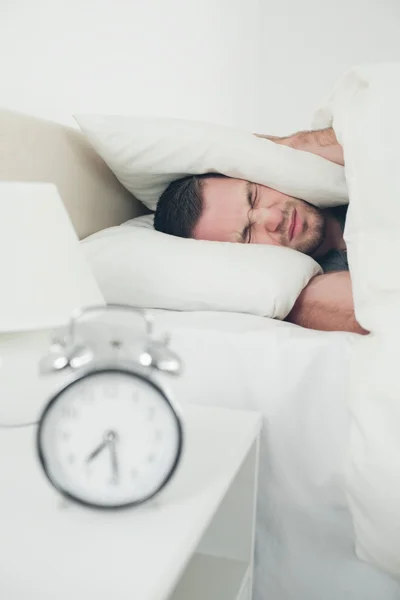 Portrait of a unhappy man covering his ears while his alarm cloc — Stock Photo, Image