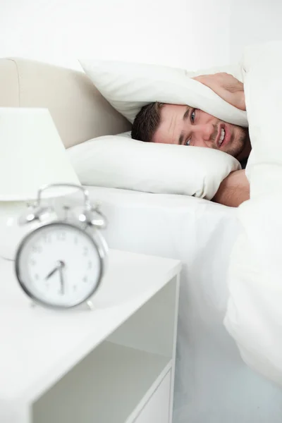 Portrait of a unhappy man covering his ears with a pillow — Stock Photo, Image