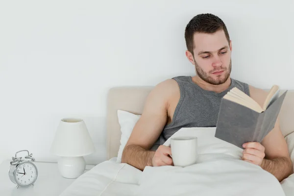 Man reading a book while holding a cup of tea — Stock Photo, Image