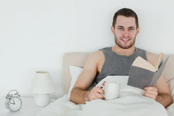 Человек, читающий роман, держа в руках чашку чая — стоковое фото