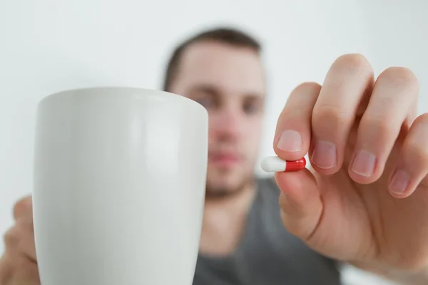 Man showing a pill and and a mug — Stock Photo, Image