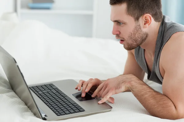 男子躺在他的肚子上的同时使用一台笔记本电脑 — 图库照片