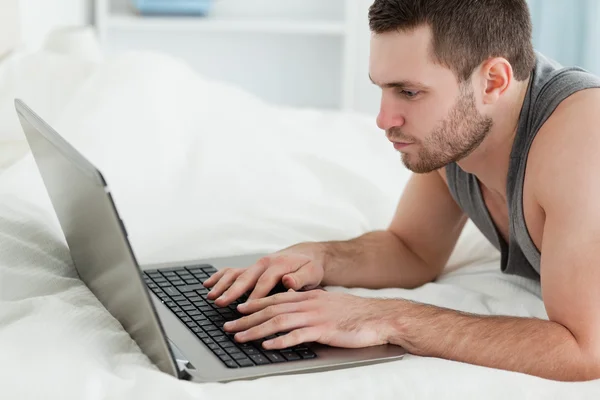 Genç adam karnı üzerinde yalan sırasında bir dizüstü bilgisayar kullanarak — Stok fotoğraf
