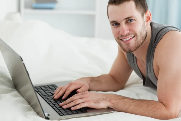 Használ egy laptop, a hasán fekve jóképű férfi — Stock Fotó