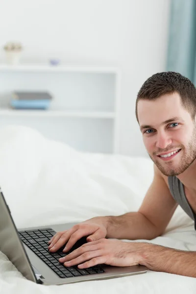 Portret van een man die een laptop gebruikt terwijl liggend op zijn buik — Stockfoto