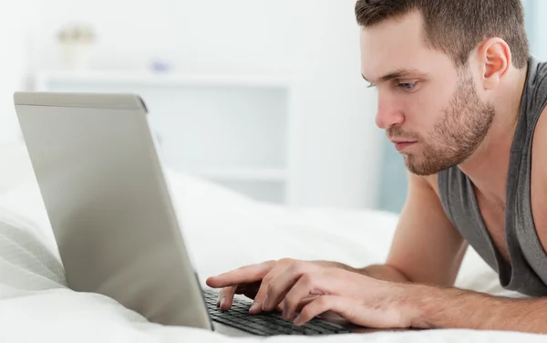 Σοβαρό άνθρωπο χρησιμοποιώντας ένα φορητό υπολογιστή ενώ βρίσκεται πάνω στην κοιλιά — Φωτογραφία Αρχείου