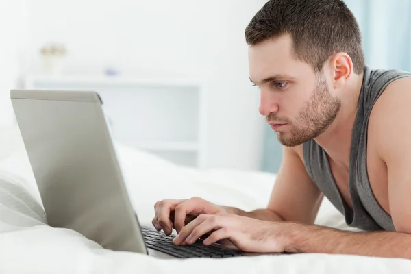 Focused man using a laptop while lying on his belly — Stock Photo, Image