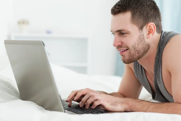 Hombre sonriente usando un portátil mientras está acostado sobre su vientre — Foto de Stock