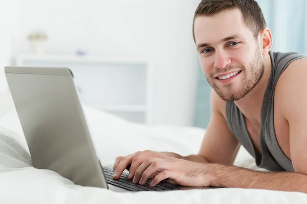 Hombre feliz usando un portátil mientras está acostado sobre su vientre — Foto de Stock