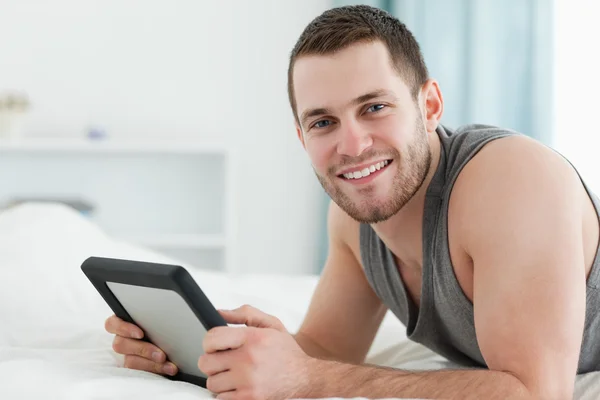 Hombre feliz usando una tableta mientras está acostado sobre su vientre —  Fotos de Stock