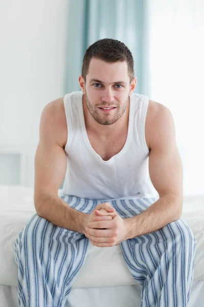Retrato de un hombre sonriente sentado en su cama — Foto de Stock