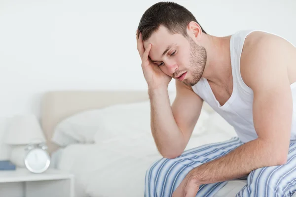 Уставший молодой человек сидит на кровати — стоковое фото