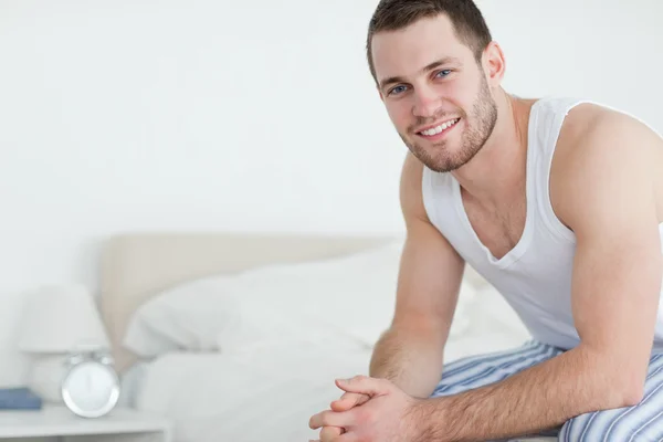 Jeune homme souriant assis sur son lit — Photo