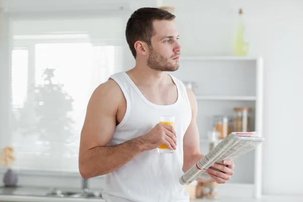 Junger Mann trinkt Orangensaft, während er Nachrichten liest — Stockfoto