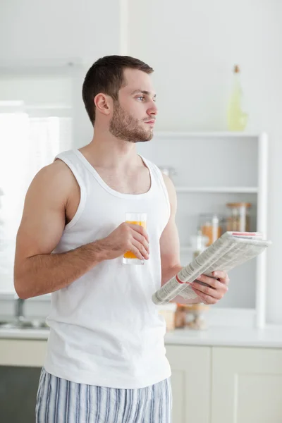 Portrait of a young man drinking orange juice while reading the — Stock Photo, Image