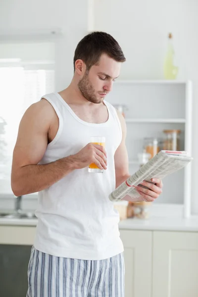 Retrato de um homem bonito bebendo suco de laranja enquanto lendo t — Fotografia de Stock
