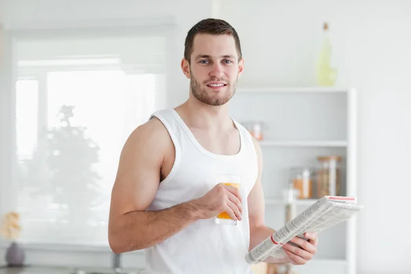 Uomo sorridente che beve succo d'arancia mentre legge le notizie — Foto Stock