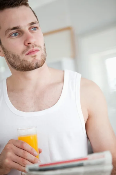 Portrait of a good looking man drinking orange juice while readi — Stock Photo, Image